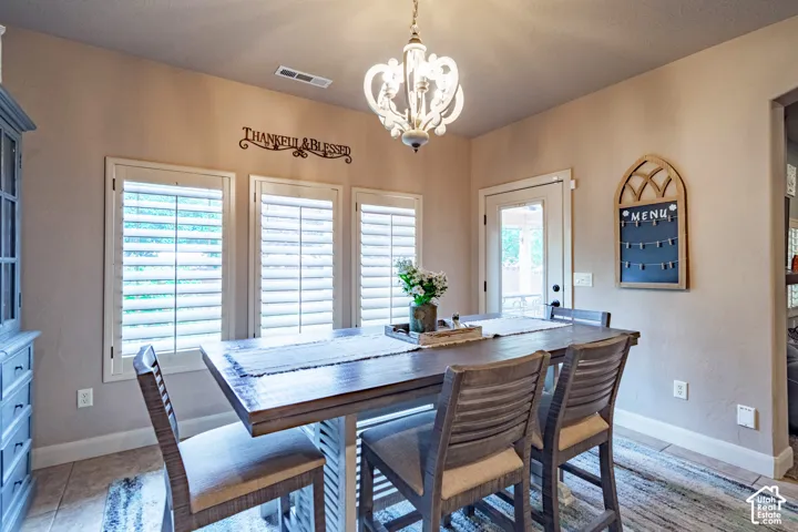 Dining area featuring a decorative chandelier, multiple windows with plantation shutters, and tiled flooring