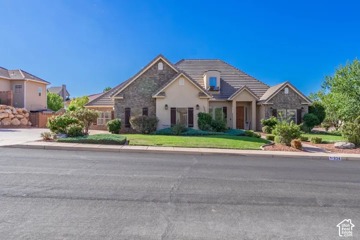 Stucco and stone exterior with a tile roof, featuring a dormer window and mature landscaping