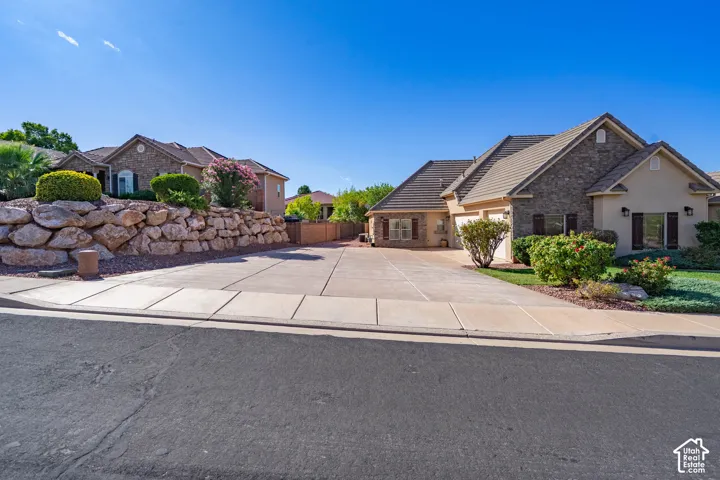 Stucco and stone exterior, multi-car driveway, tile roofing, mature landscaping, and an integrated garage