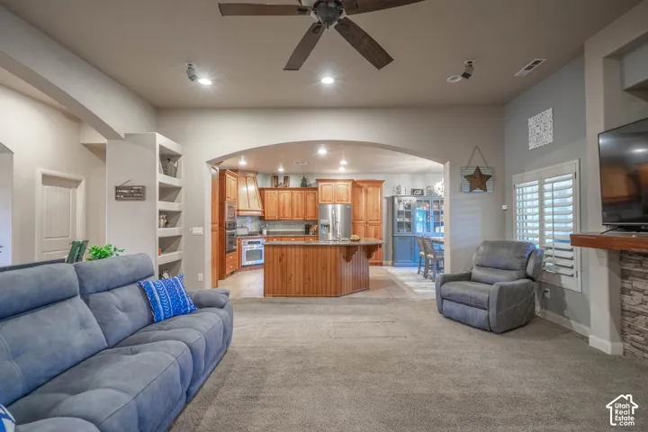 Archway entry to the kitchen, stone-clad fireplace, wood-finish ceiling fan, and built-in shelving