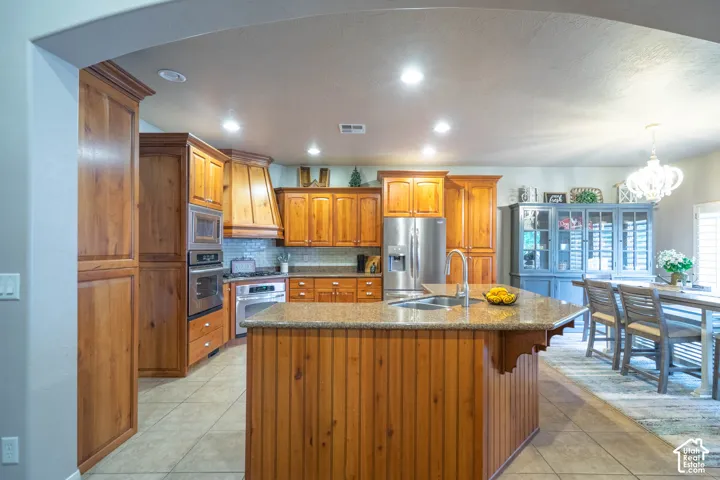 Kitchen featuring a central island with a built-in sink, wood-finish cabinetry, stainless steel appliances, and recessed lighting