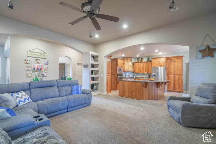 Carpeted living area with arched doorway, built-in shelving, ceiling fan, and recessed lighting