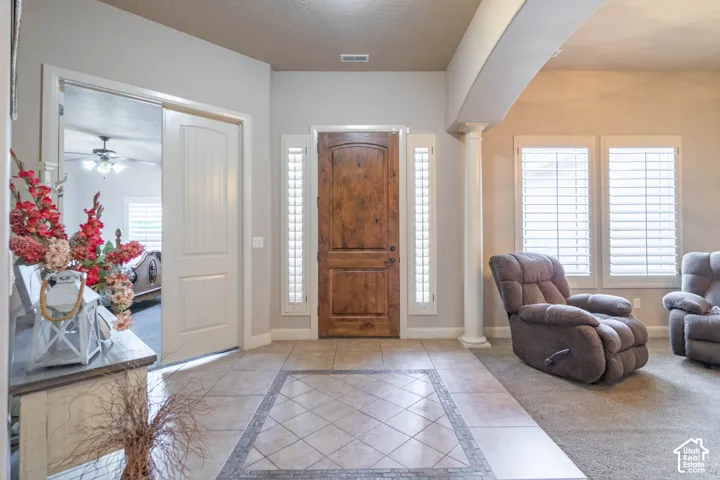 Hardwood entry door with sidelights, tile flooring with mosaic inlay, structural column, and multiple windows with plantation shutters