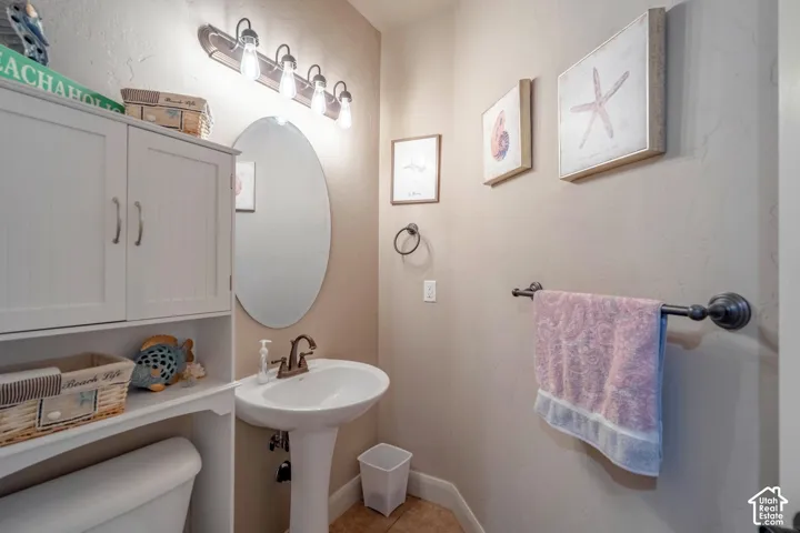 Pedestal sink with bronze-finish faucet, oval mirror, and wall-mounted vanity lighting