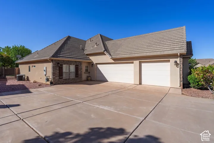 Stucco exterior with stone accents, a tile roof, two garage doors, and a concrete driveway