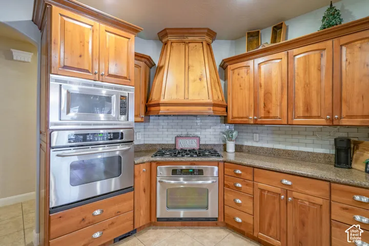 Wood-finish cabinetry with decorative crown molding, stainless steel built-in appliances, a gas cooktop, and a subway tile backsplash