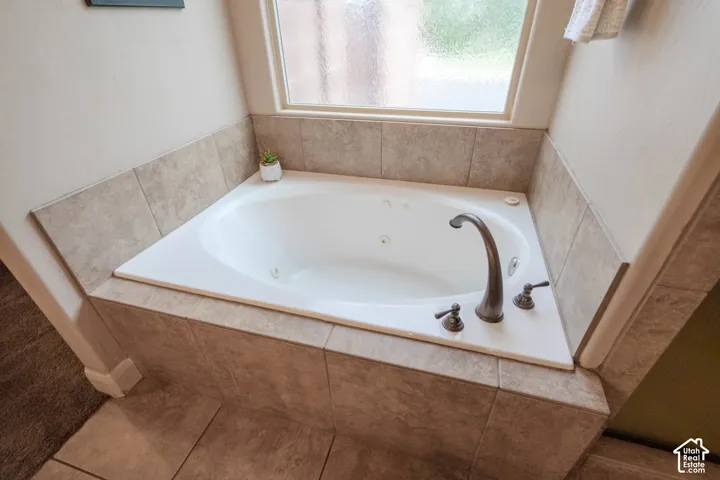 Jetted soaking tub with bronze-finish fixtures, set within a tiled surround and featuring a privacy window