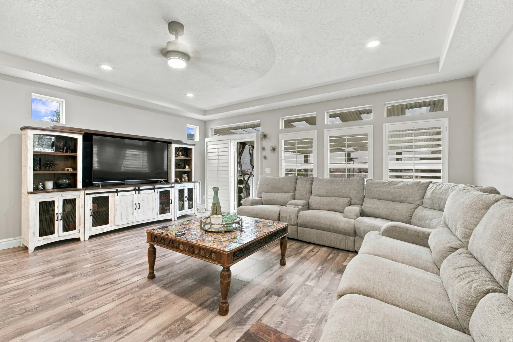 Wood-finish flooring with a multi-pane window wall, transom windows, and white plantation shutters