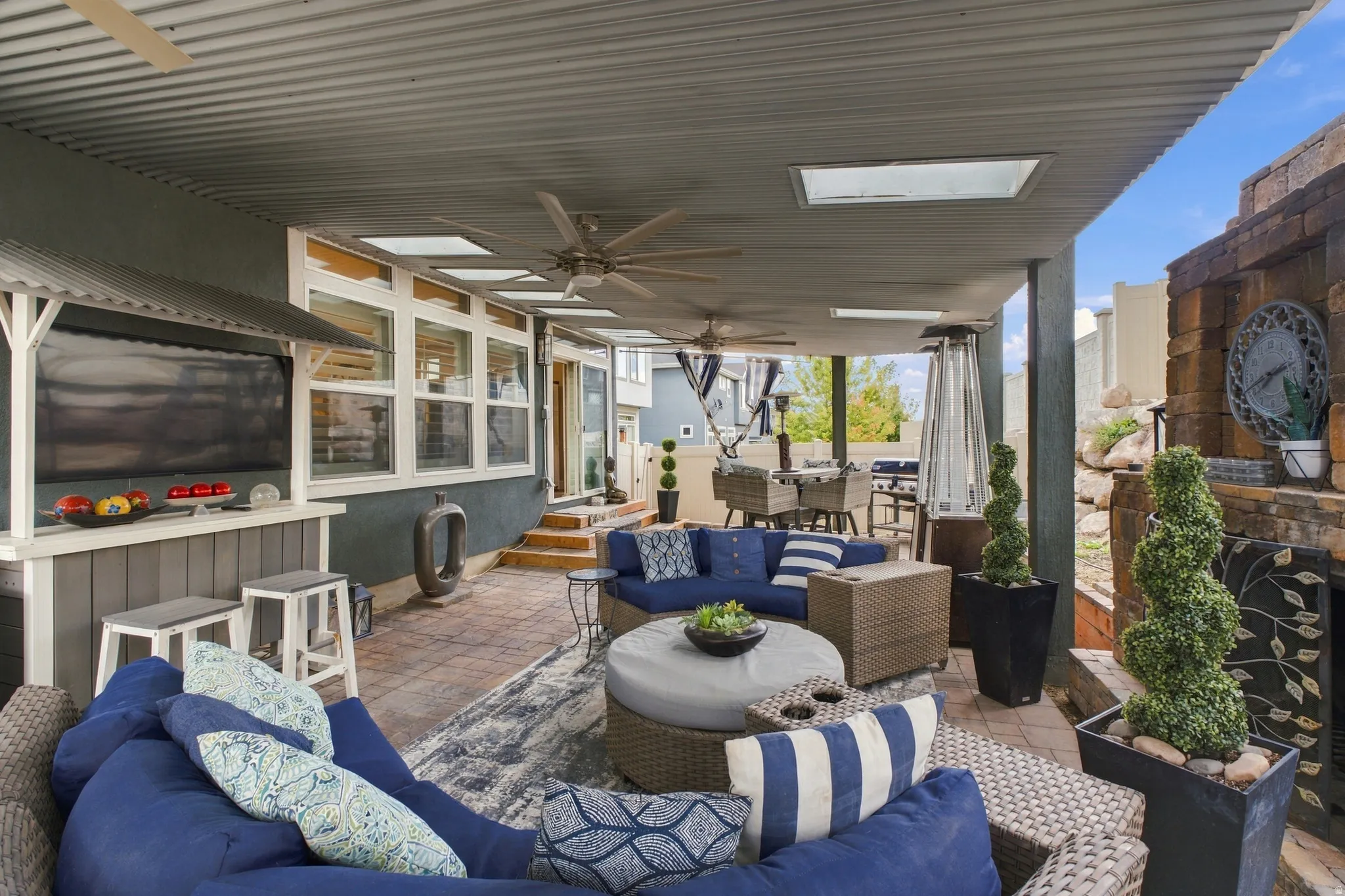 Covered patio featuring a corrugated metal ceiling, skylights, outdoor bar area, brick fireplace, and paver flooring