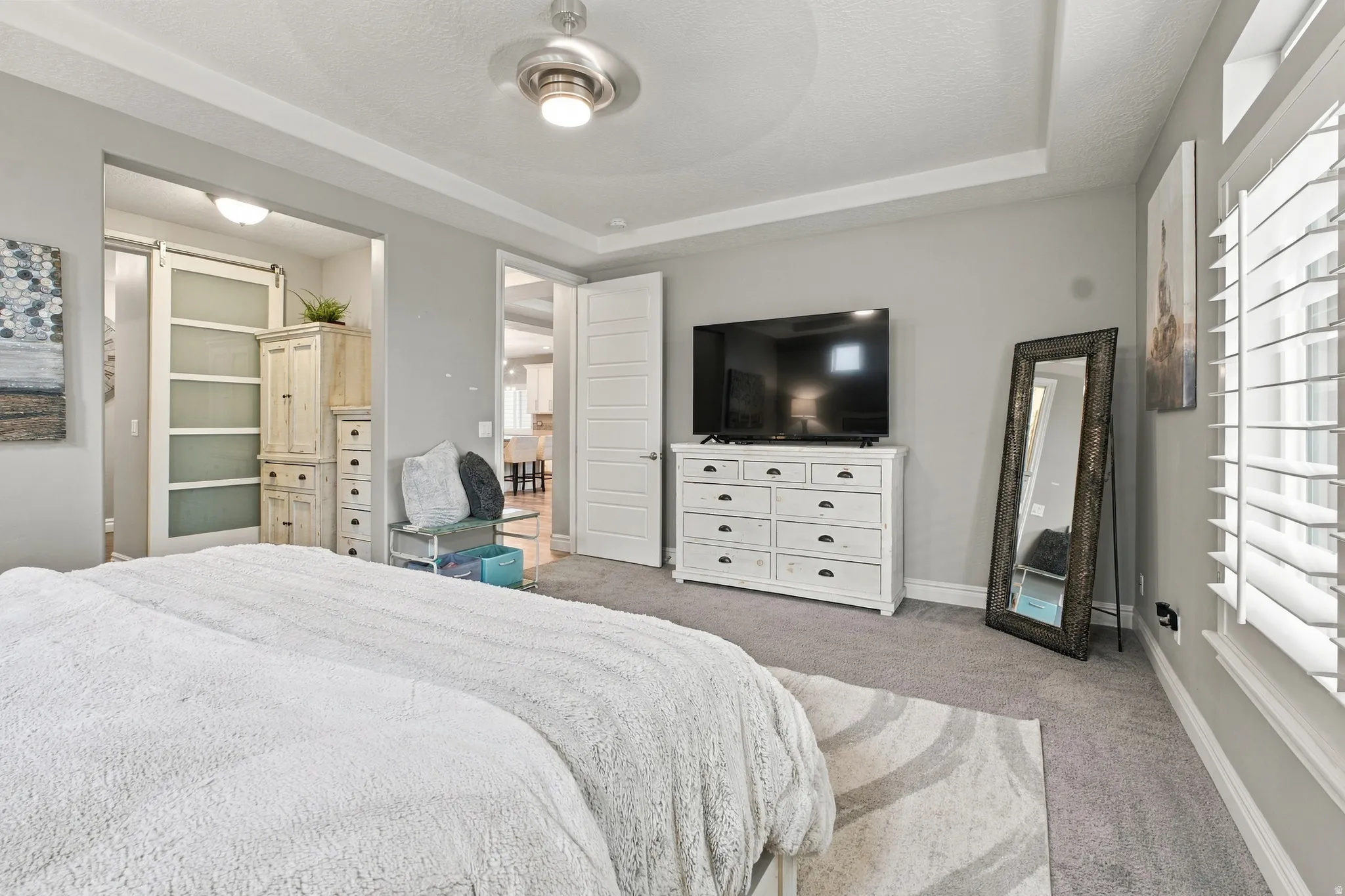 Tray ceiling with a ceiling fan, plantation shutters, and carpeted flooring