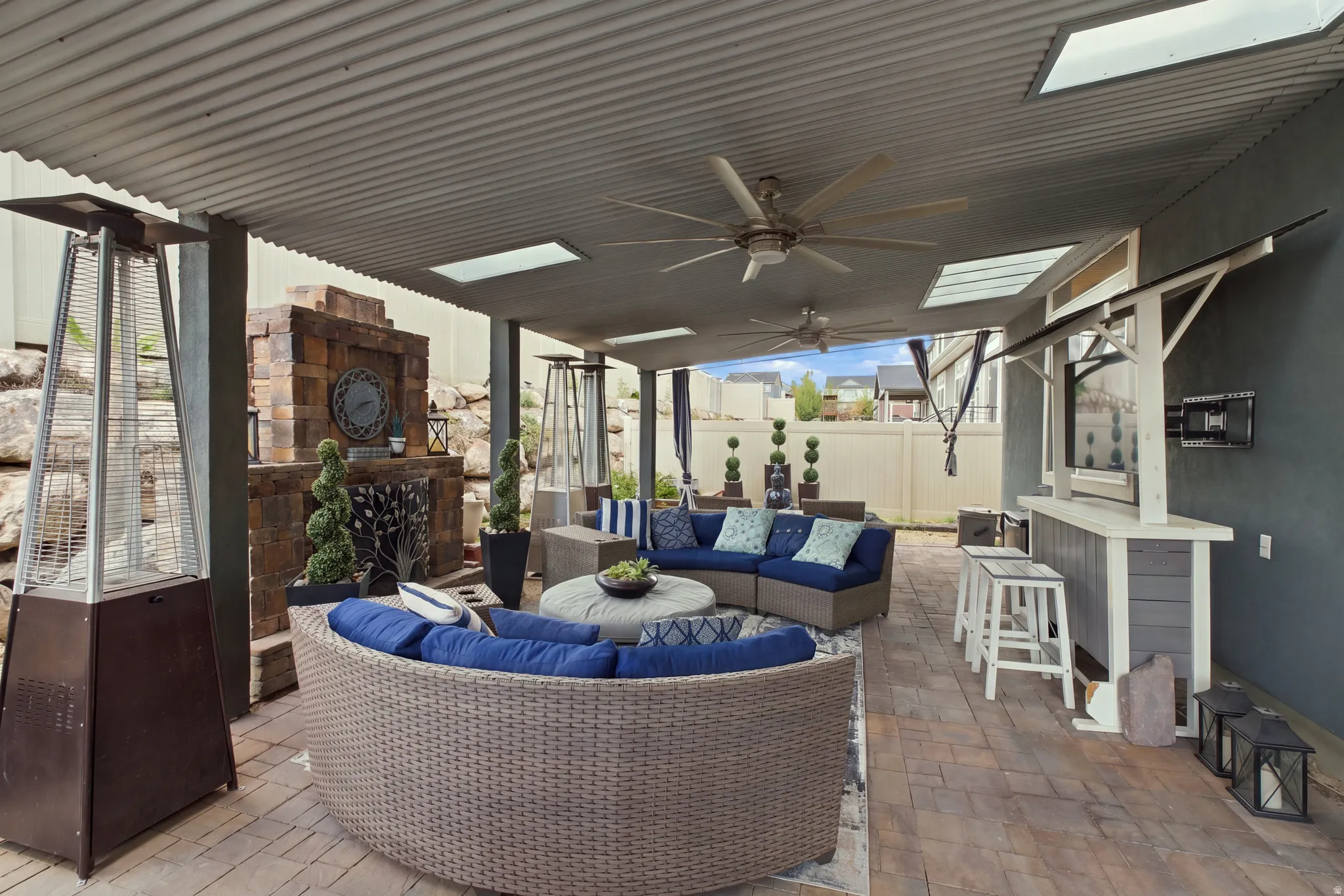 Covered patio featuring a corrugated metal roof, skylights, ceiling fans, a stone fireplace, and a built-in bar