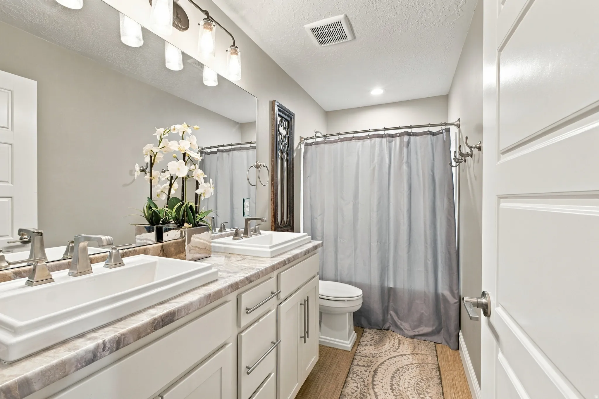 Dual vessel sinks, stone-finish countertop, brushed nickel fixtures, wood-finish flooring, and a full bath with a shower/tub combination