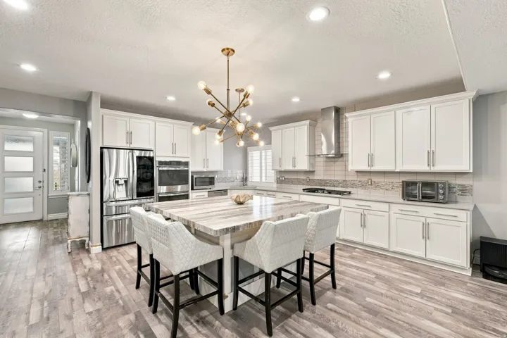 Spacious kitchen featuring white cabinetry, stainless steel appliances, a center island with seating, a decorative chandelier, and wood-finish flooring