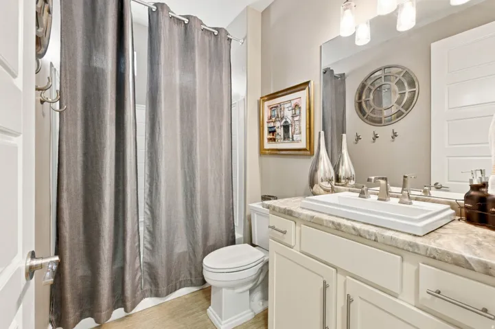 White shaker-style vanity with brushed nickel pulls, a rectangular vessel sink, and a stone-finish countertop
