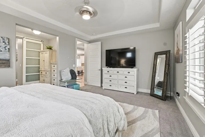 Tray ceiling with a ceiling fan, plantation shutters, and carpeted flooring