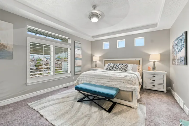 Tray ceiling with a ceiling fan, wall-mounted light fixtures, built-in window shutters, and carpet flooring