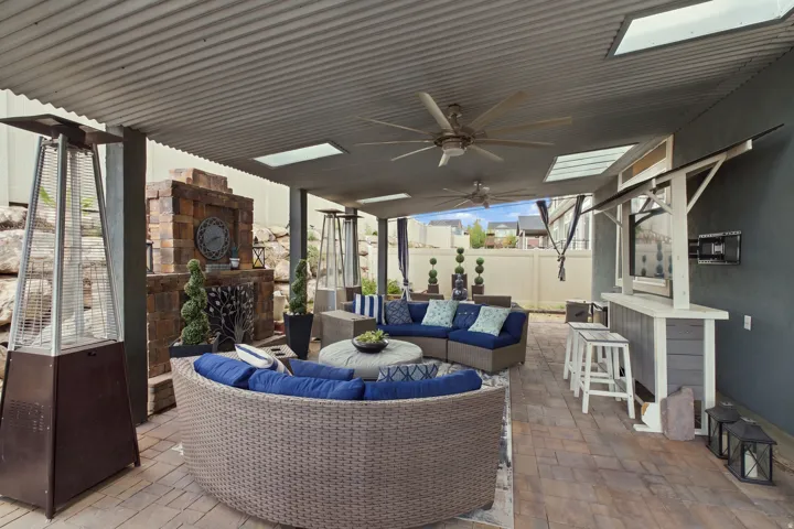 Covered patio featuring a corrugated metal roof, skylights, ceiling fans, a stone fireplace, and a built-in bar
