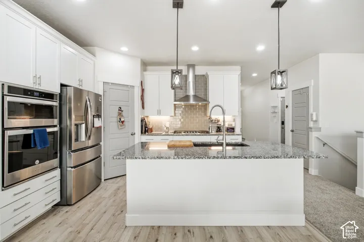 Kitchen featuring an expansive island with a granite countertop, white cabinetry with silver hardware, wood-finish flooring, a stainless steel double oven, and pendant lighting