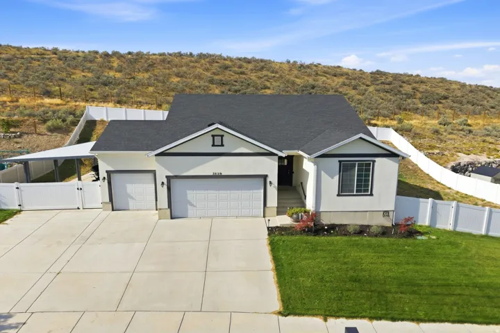 Stucco exterior with dark trim accents, attached two-car garage, paved driveway, carport, and white privacy fencing