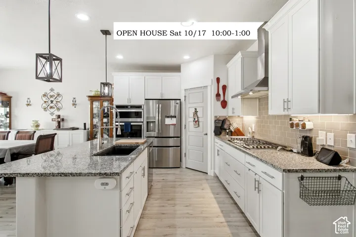 Kitchen featuring white cabinetry, stone countertops, stainless steel appliances, a center island with a basin sink, and wood-finish flooring