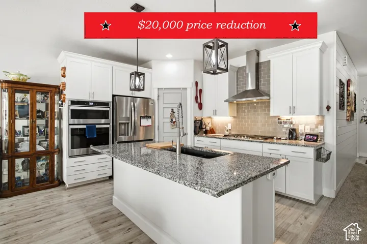 Kitchen featuring a stone-topped island with an undermount sink, white shaker-style cabinetry, stainless steel double wall ovens, a tile backsplash, and overhead lantern-style pendant lighting