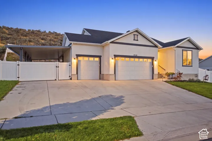 Stucco exterior with dark trim accents, two-car garage, covered carport, concrete driveway, and white privacy fencing
