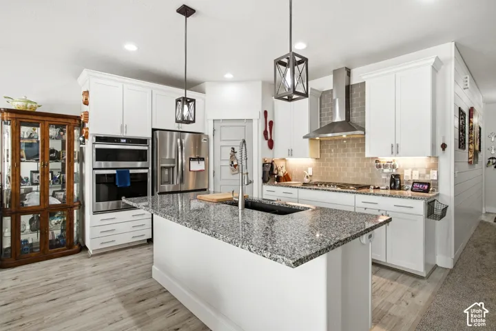 Kitchen featuring white cabinetry, wood-finish flooring, a central island with a dark sink, granite-style countertops, and stainless steel appliances