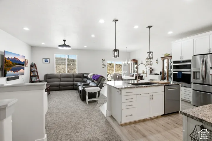 Open-concept layout featuring a kitchen island with sink, stainless steel appliances, white cabinetry, and wood-finish flooring