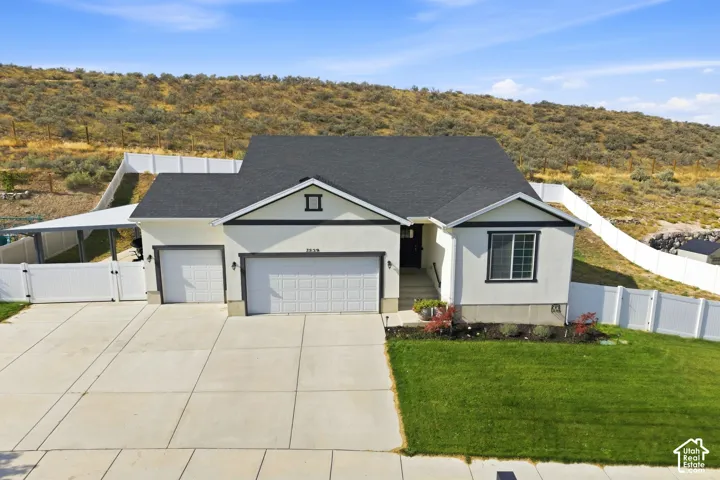 Stucco exterior with dark trim accents, attached two-car garage, paved driveway, carport, and white privacy fencing