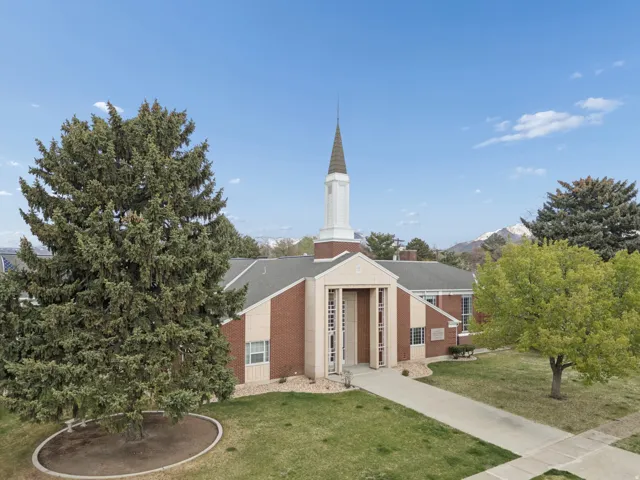 Brick exterior with a prominent steeple, paved walkways, mature trees, and a landscaped front area
