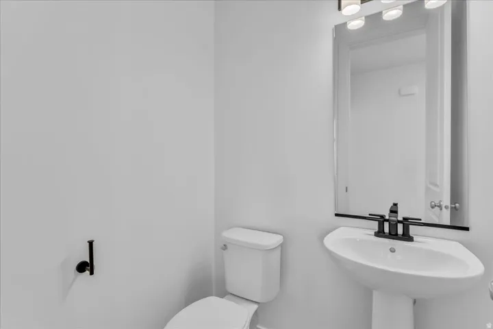 Pedestal sink with matte black faucet, wall-mounted mirror, and contemporary vanity lighting