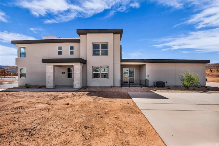 Modern exterior with stucco finish, contrasting dark trim, stone-clad entryway columns, and multiple large windows