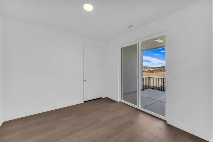 Recessed lighting, wood-finish flooring, white walls, white paneled door, and a sliding glass door to a concrete patio with a black metal railing