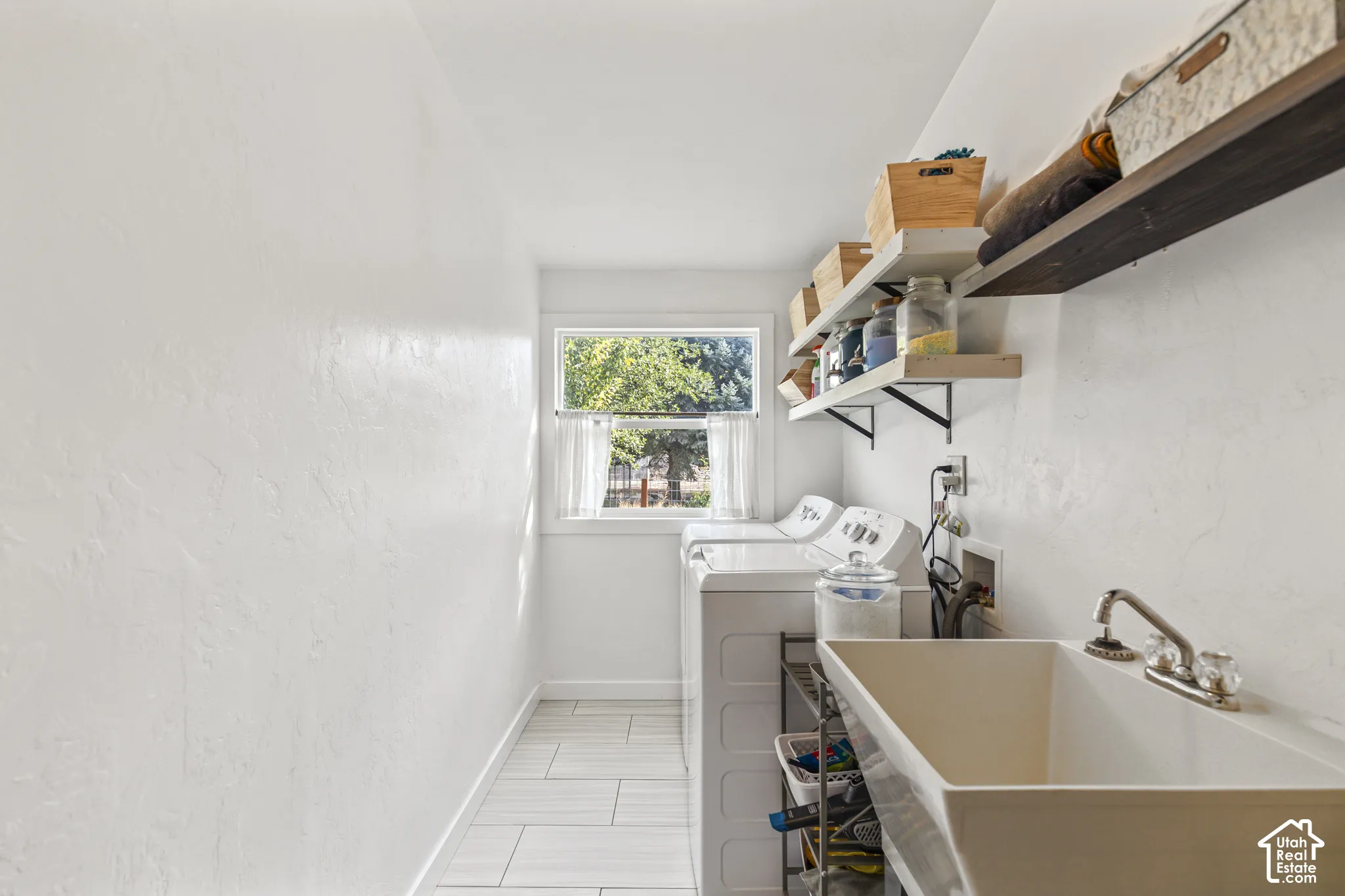 White utility sink with dual-handle faucet, window with natural light, and floating shelves