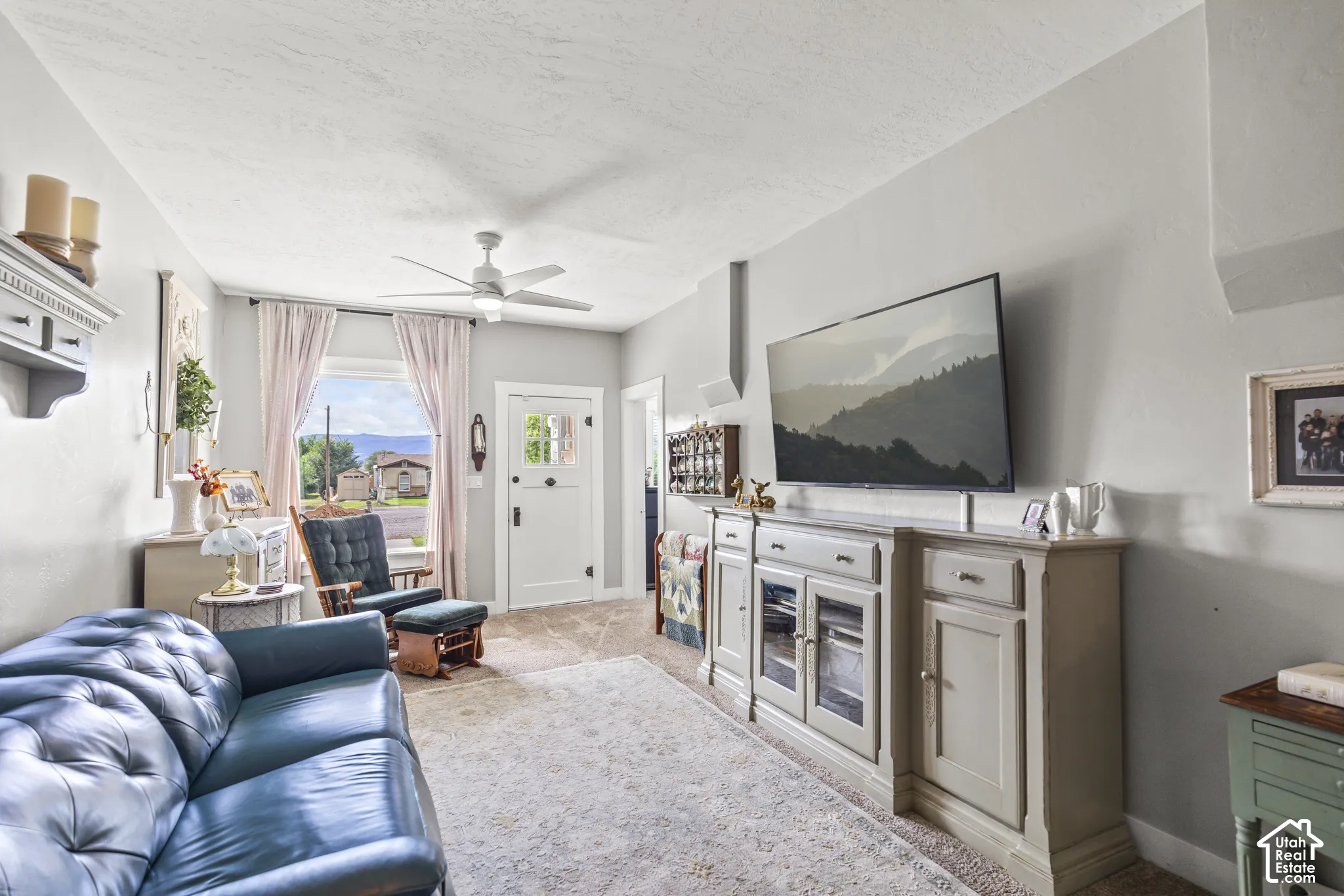 Bright living area with a ceiling fan, light-toned walls, and a window with white trim