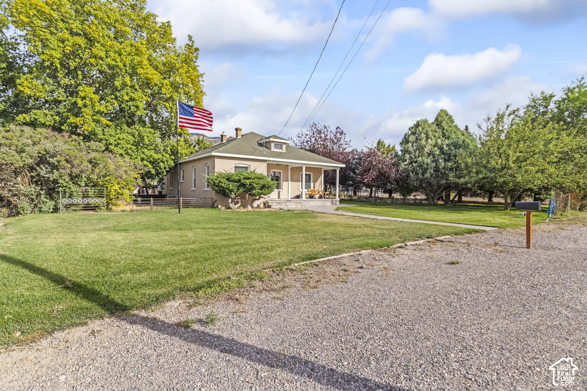 Property exterior featuring a gravel driveway, expansive lawn, mature landscaping, and a covered porch