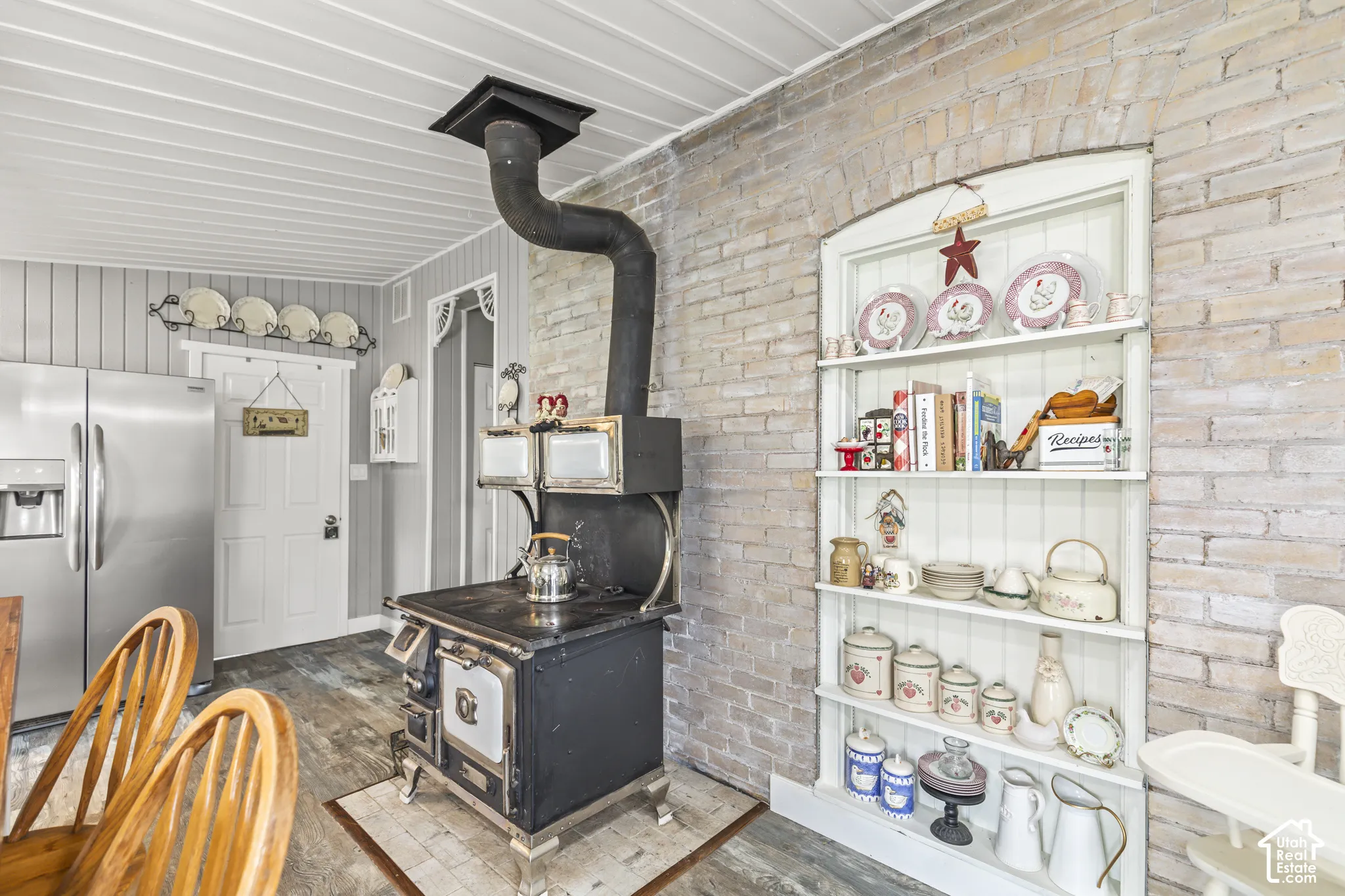 Exposed brick accent wall, wood-finish flooring, beadboard wall paneling, built-in shelving, and a freestanding wood-burning stove