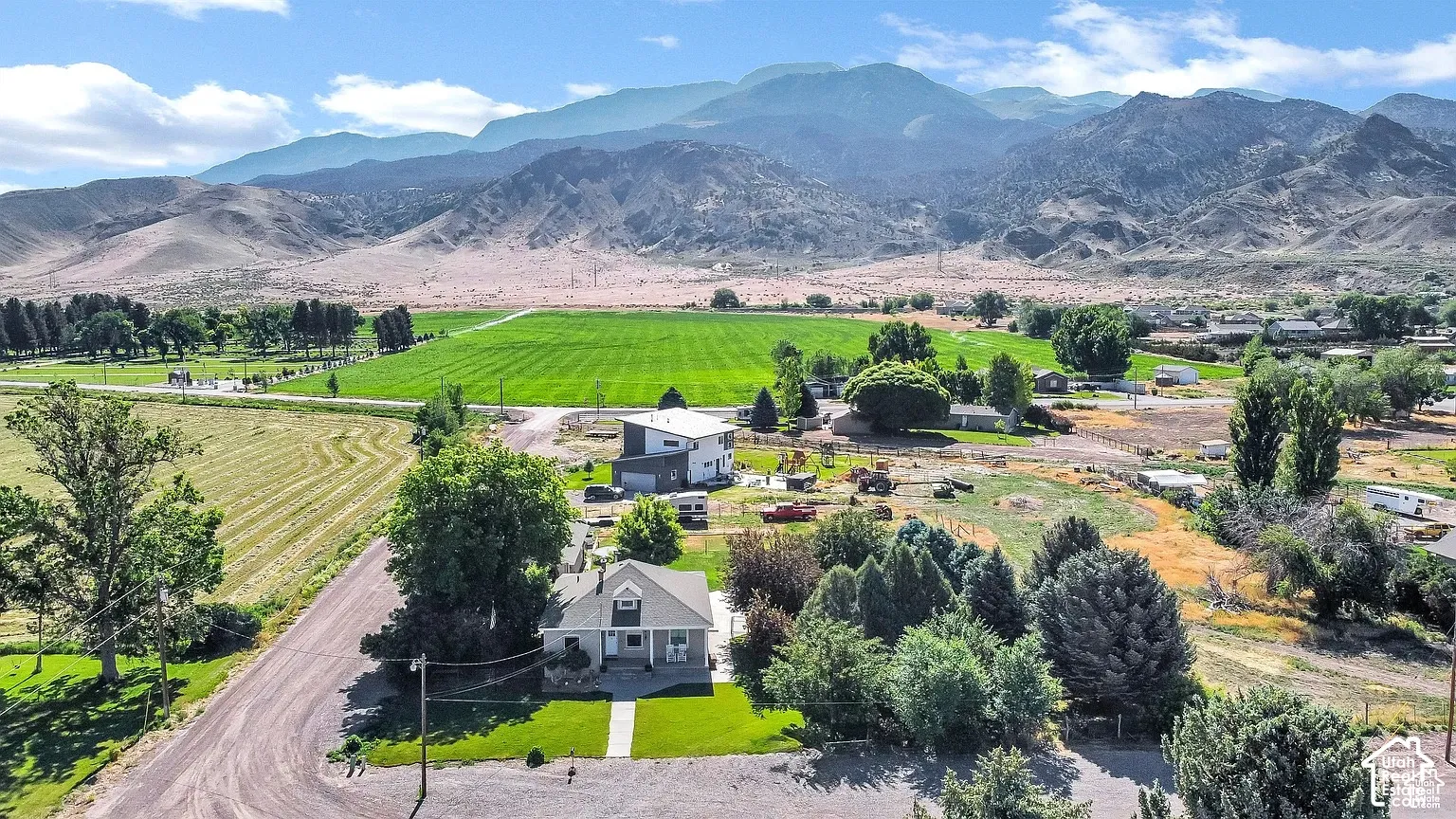 Expansive property with a gabled roofline, mature trees, and a manicured lawn, set against a mountainous backdrop with distant green fields