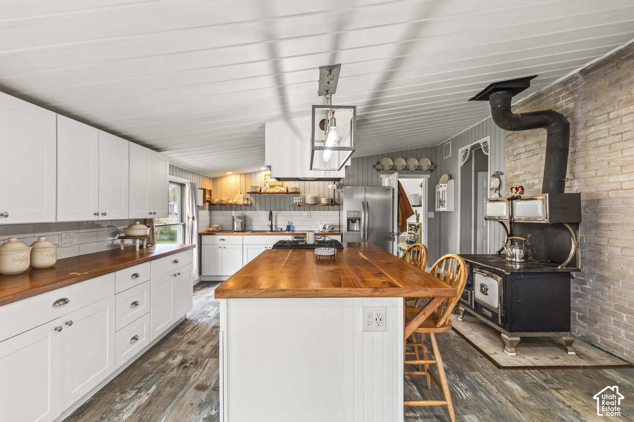 White cabinetry with wood-finish countertops, subway tile backsplash, and a central island with breakfast bar seating