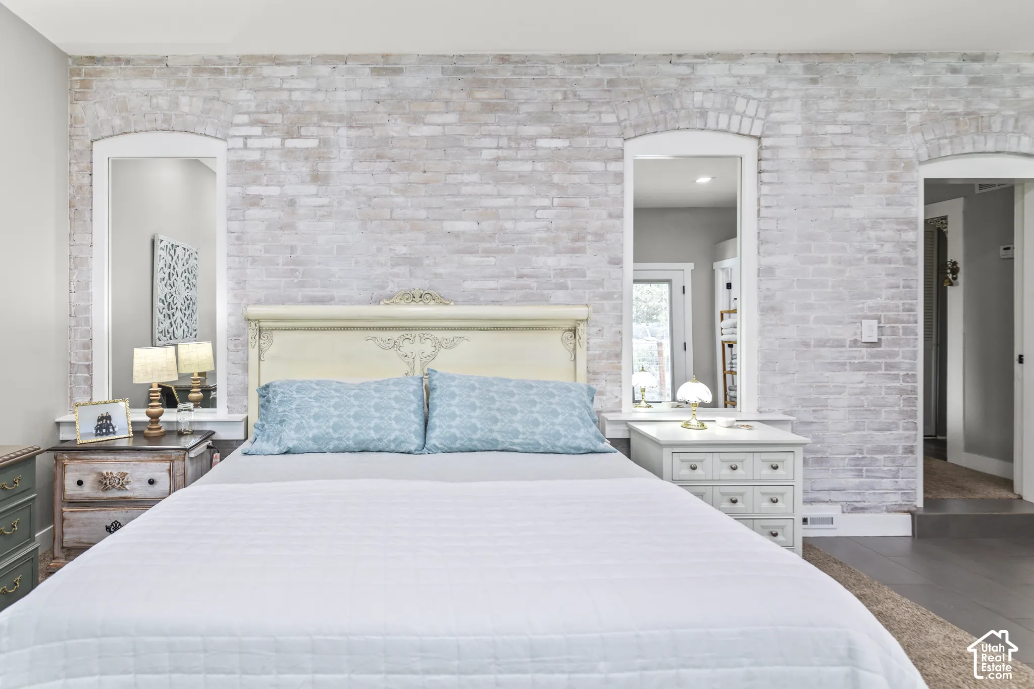 Exposed brick wall with a whitewashed finish, arched mirror niches, and a decorative headboard