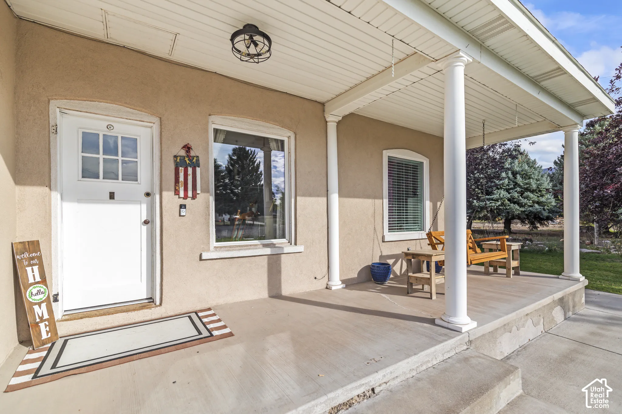 Covered front porch with white columns, stucco exterior finish, recessed lighting, and a white paneled entry door with windowpanes