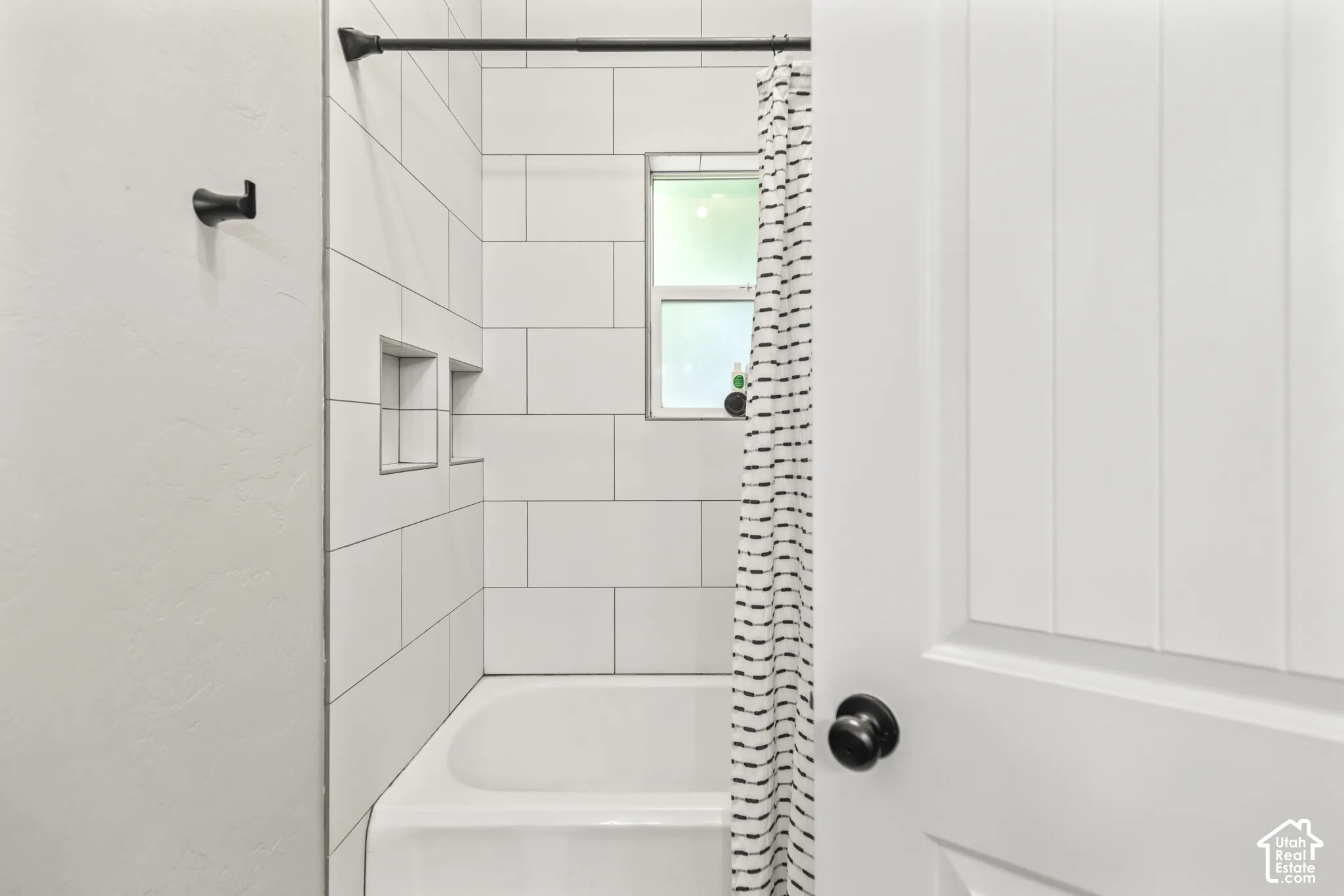 Bathtub with white subway tile surround, two tiled shower niches, and a window for natural light