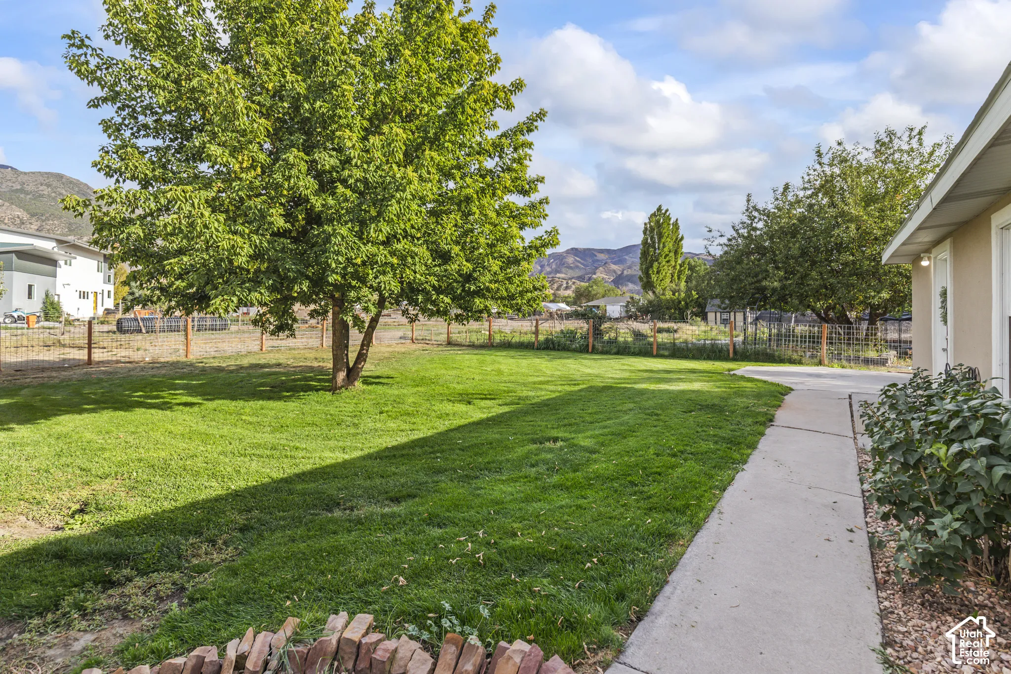 Expansive lawn area with mature trees, defined by a wood and wire fence, featuring a concrete pathway
