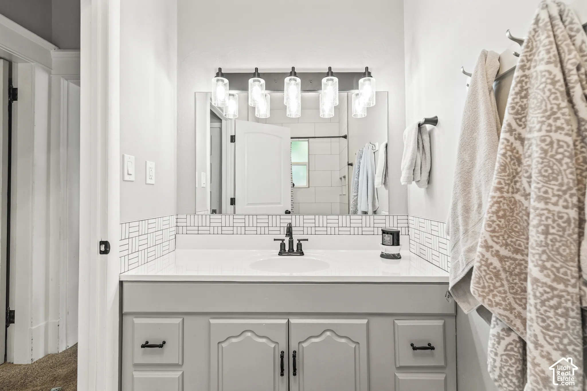 White vanity with a single basin sink, matte black faucet, and patterned tile backsplash