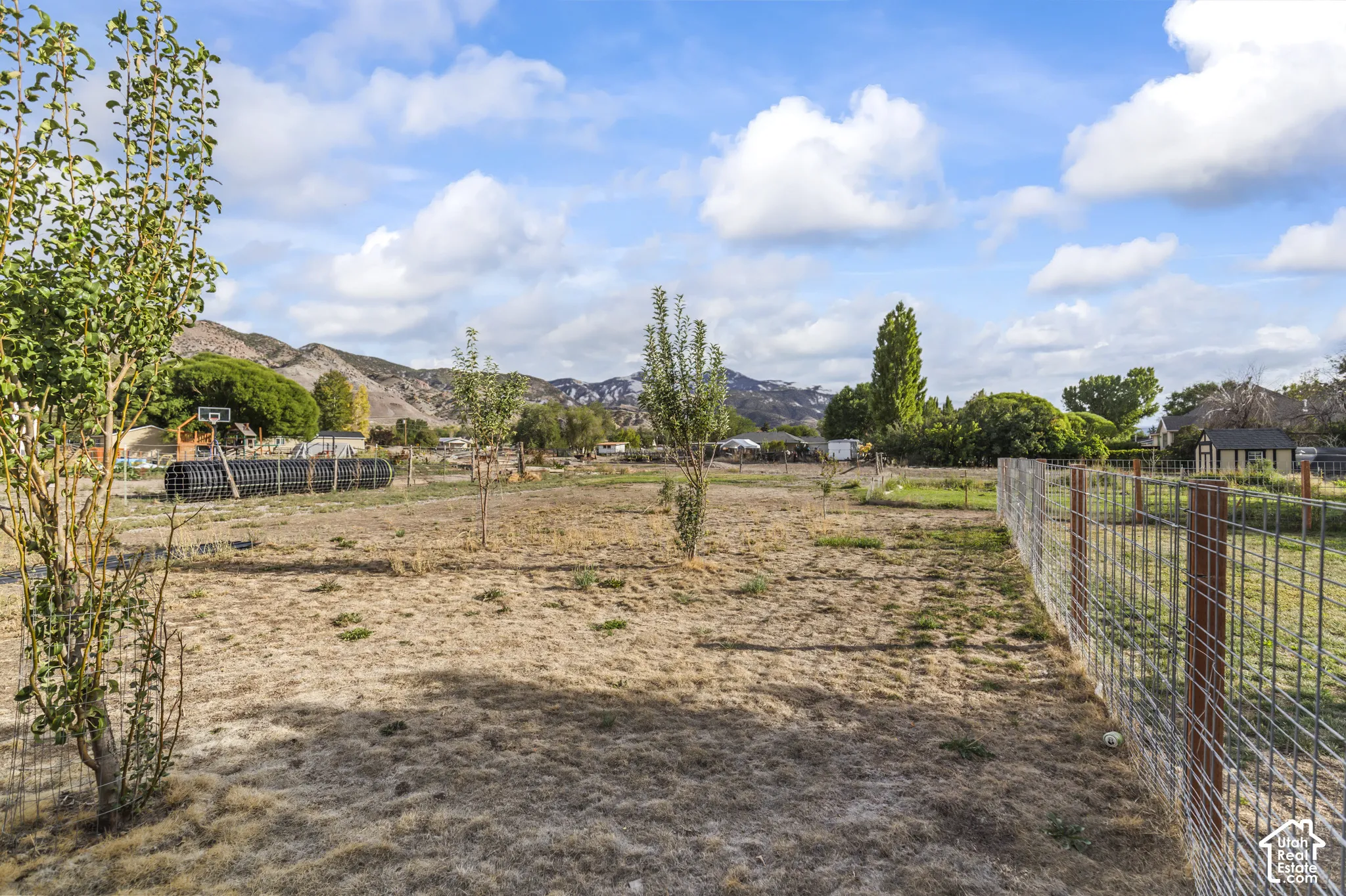 Expansive lot featuring a wire fence, natural ground cover, and surrounding hills