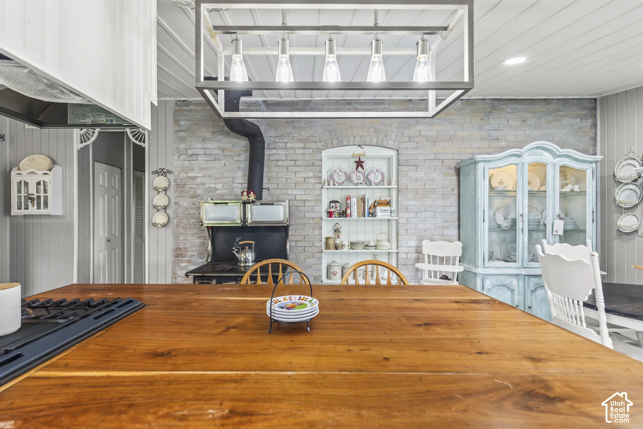 Wood-finish countertop with an integrated cooktop, exposed brick accent wall, white wood paneling, and an overhead rectangular light fixture