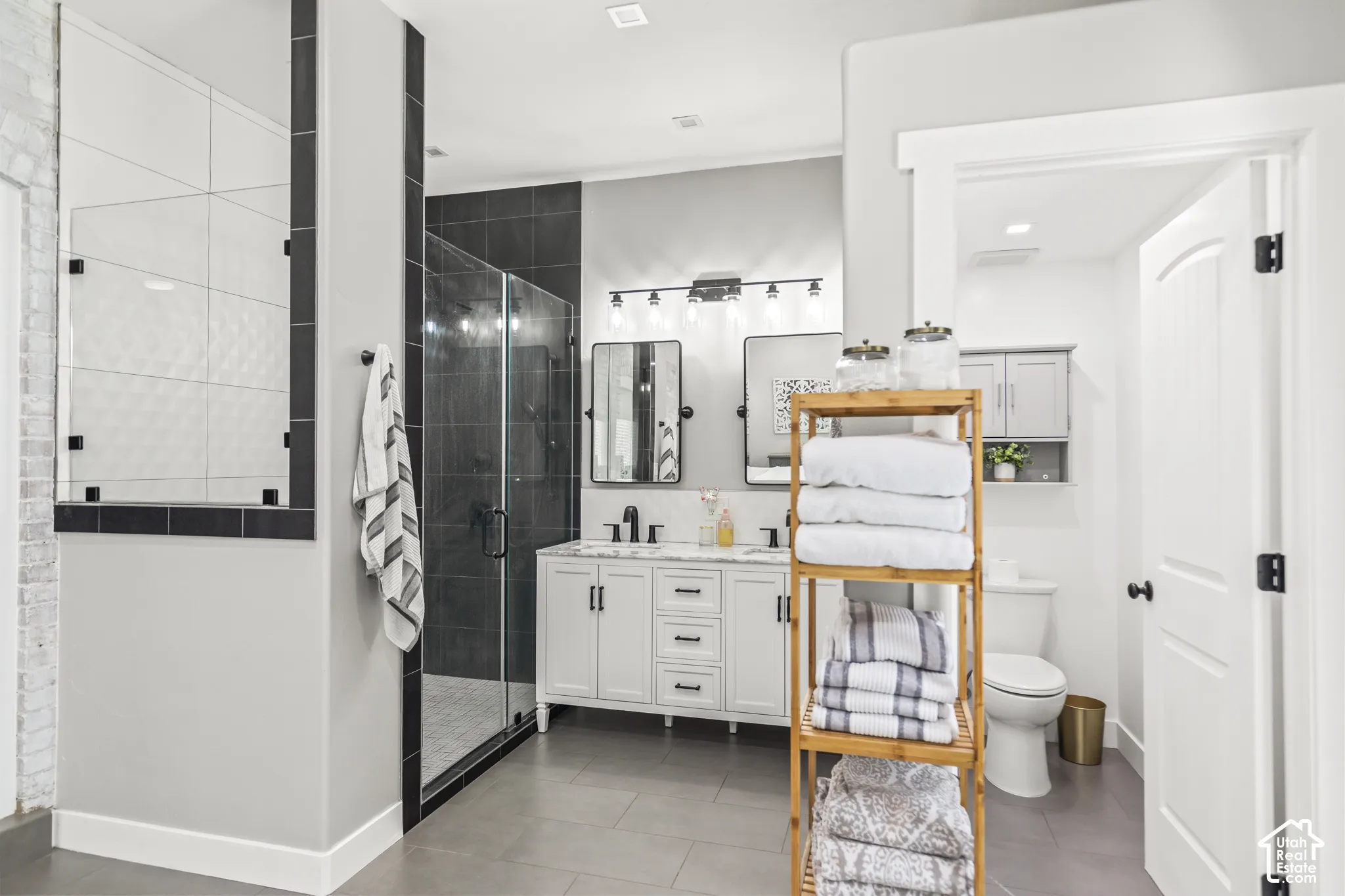 Dual vanity with quartz countertop, walk-in shower with glass enclosure, tiled shower walls, and gray floor tiling