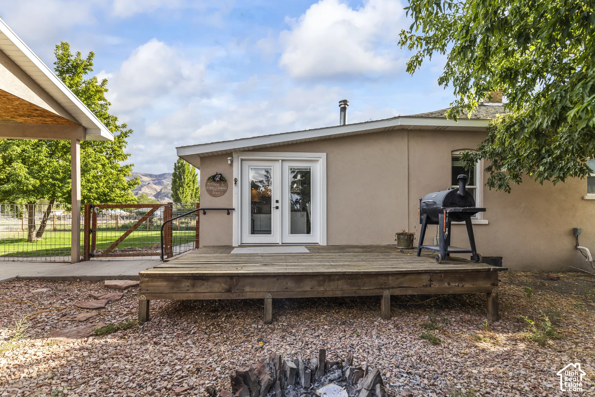Charming single-story residence featuring a spacious gravel-surfaced outdoor entertaining area with a composite deck, mature landscaping with established trees, and a built-in grill