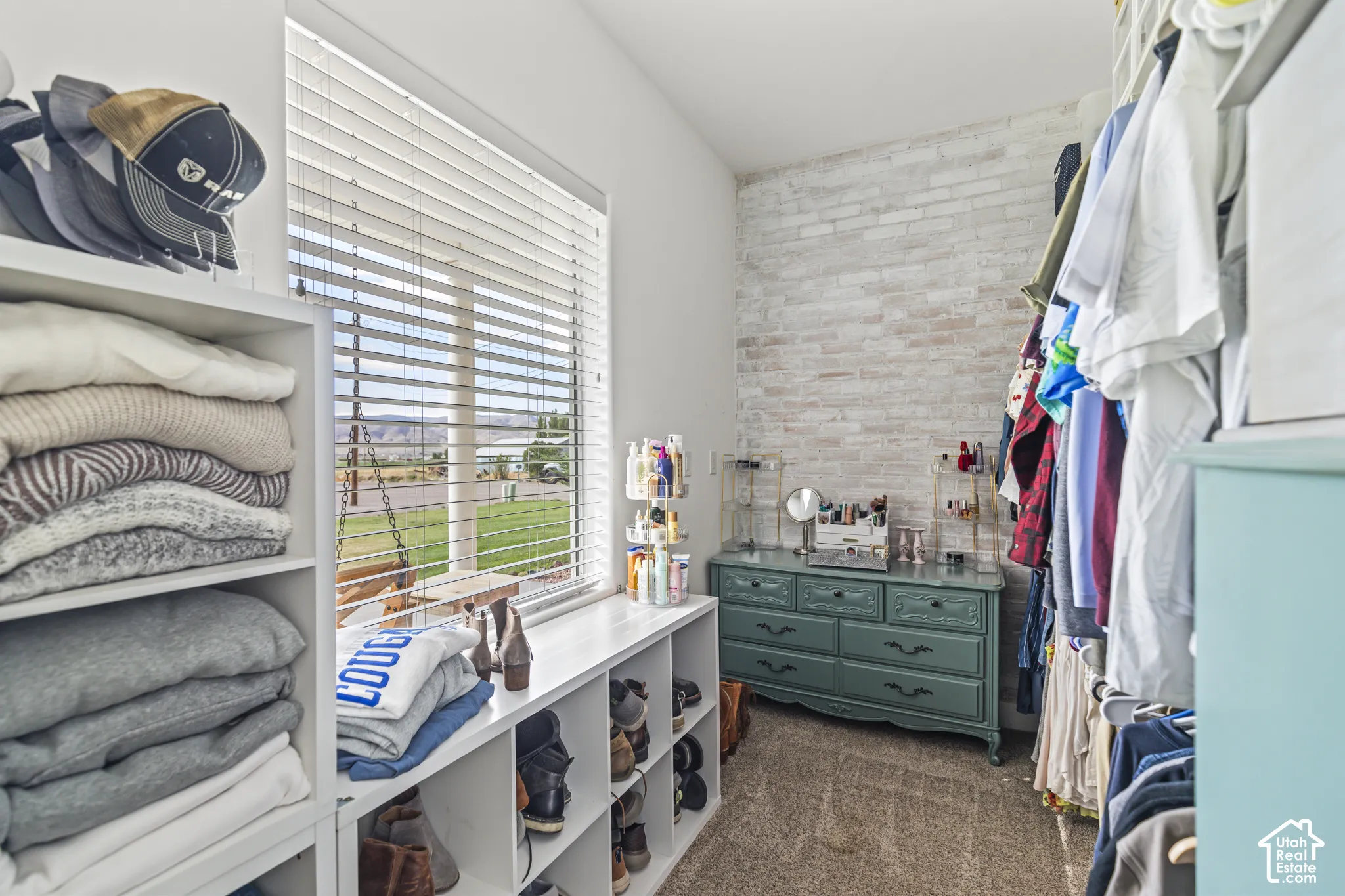 Built-in white shelving, window with blinds, light-colored brick accent wall, and carpeting