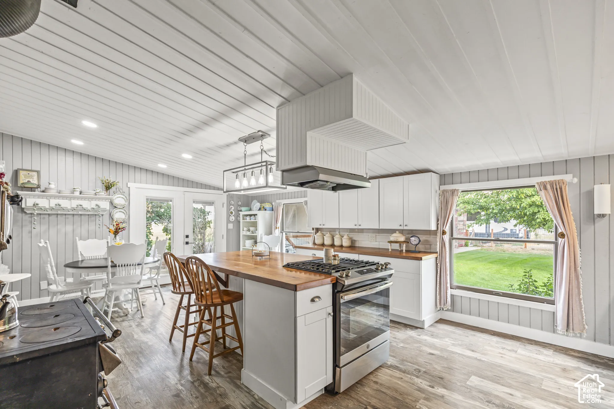 Kitchen featuring wood-finish flooring, white cabinetry, a wood countertop island with seating, a gas range with a range hood, and a window overlooking a grassy area